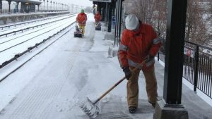 Snow removal workers clearing snow and ice from sidewalks at a Toronto GO train station platform.