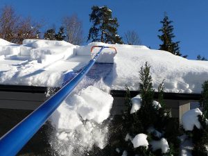 Extended roof snow removal tool pulling snow off a residential roof to prevent buildup and damage.