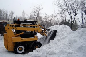 Small bobcat loader piling snow to the side of a residential neighborhood street.