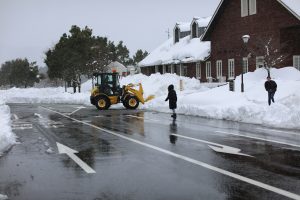 Snow plow truck clearing street and sidewalk near a local city school with precise, efficient snow removal.